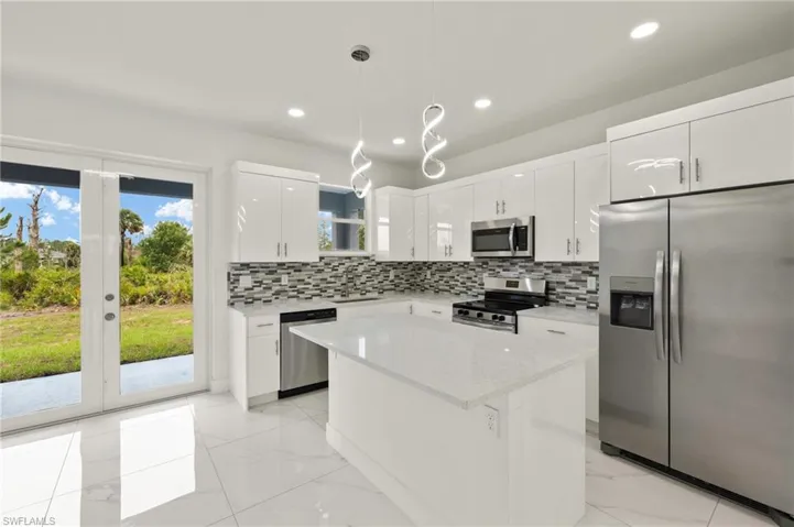 Kitchen with appliances with stainless steel finishes, decorative backsplash, decorative light fixtures, a kitchen island, and white cabinets