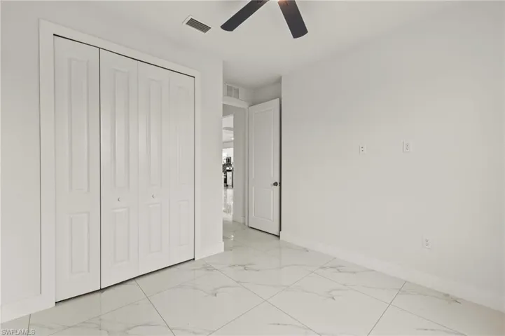 Unfurnished bedroom featuring light marble finish flooring, baseboards, a closet, and a ceiling fan