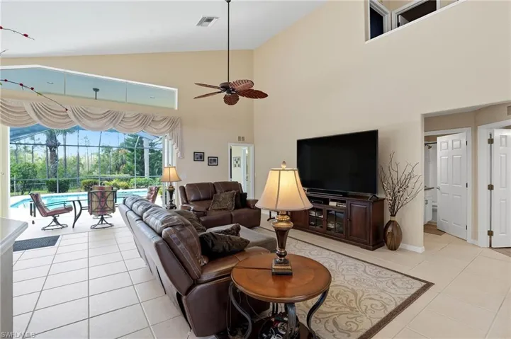 Living room featuring high vaulted ceiling, light tile patterned floors, lanai access, and ceiling fan