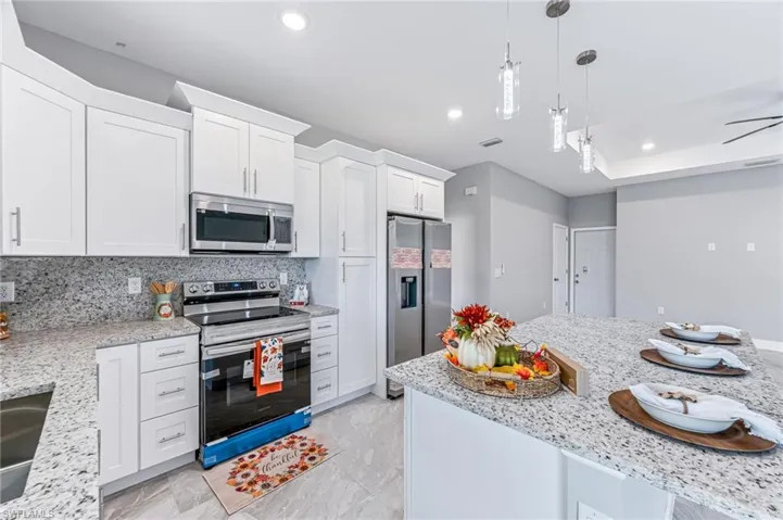 Kitchen featuring white cabinets, decorative backsplash, light stone countertops, and stainless steel appliances