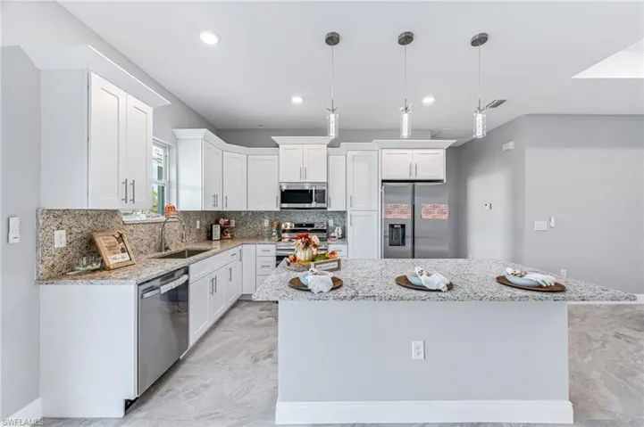 Kitchen with appliances with stainless steel finishes, white cabinetry, a kitchen island, and sink