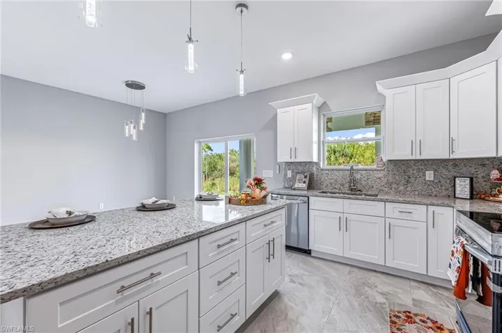 Kitchen with white cabinets, sink, appliances with stainless steel finishes, tasteful backsplash, and decorative light fixtures
