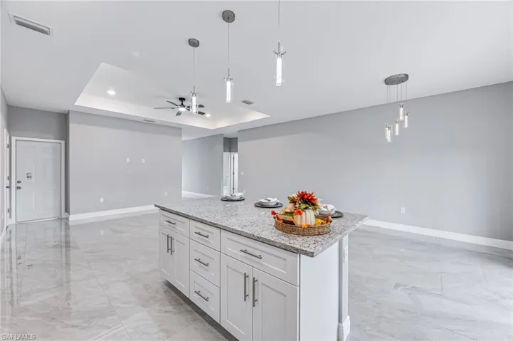 Kitchen featuring a raised ceiling, hanging light fixtures, ceiling fan, light stone countertops, and white cabinetry