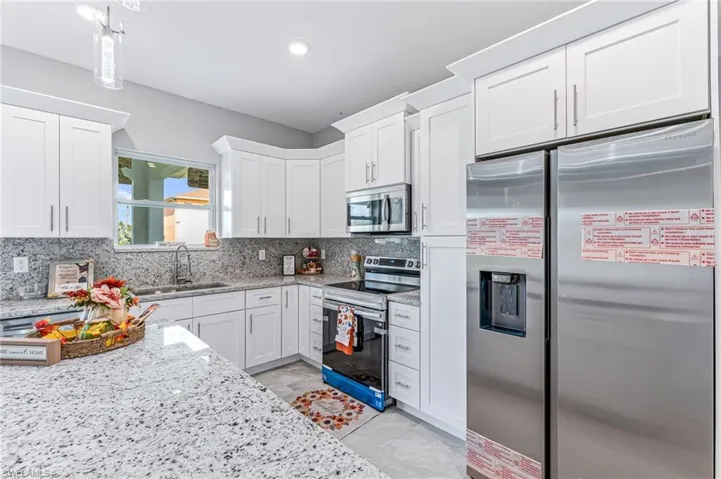 Kitchen with white cabinets, backsplash, sink, and appliances with stainless steel finishes