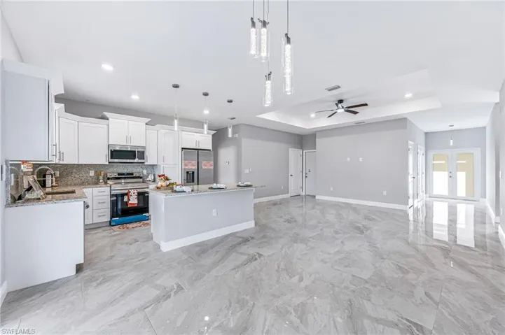 Kitchen featuring appliances with stainless steel finishes, a center island, decorative light fixtures, and a tray ceiling