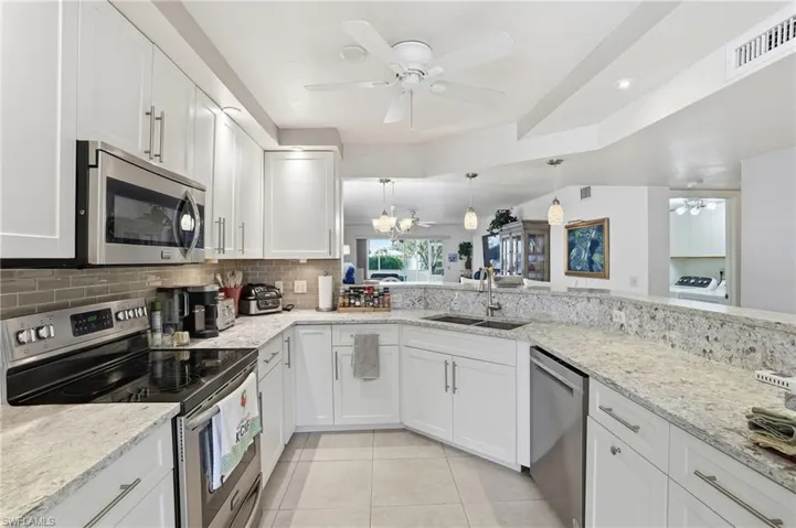 Kitchen with stainless steel appliances, ceiling fan, white cabinetry, light tile patterned floors, and light stone countertops