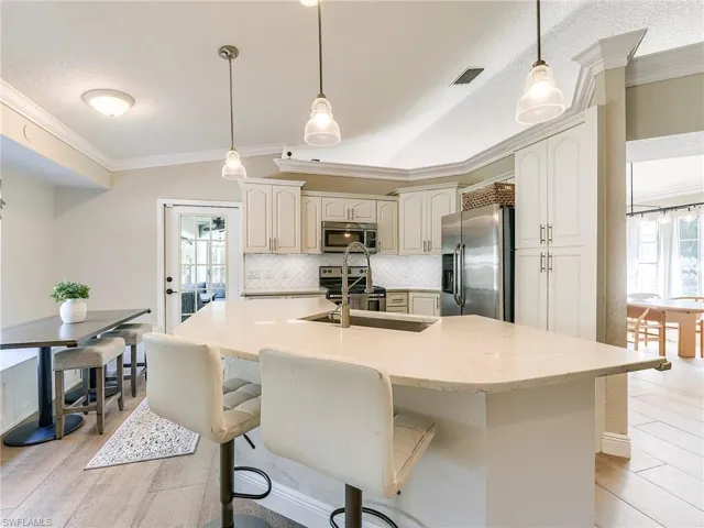 Kitchen with crown molding, stainless steel appliances, tasteful backsplash, hanging light fixtures, and a center island with sink