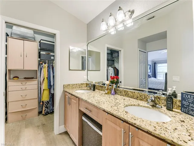 Bathroom featuring double vanity, ensuite bathroom, a walk in closet, and light wood-style floors