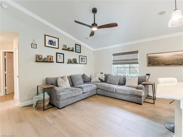 Living area with ornamental molding, lofted ceiling, ceiling fan, and light wood-type flooring