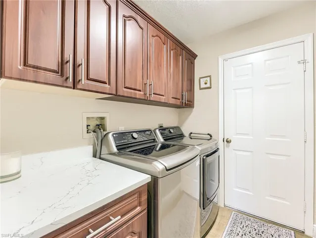 Laundry area with washer and clothes dryer, cabinet space, and a textured ceiling
