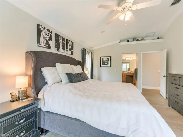 Bedroom featuring vaulted ceiling, crown molding, light wood-style flooring, and a ceiling fan