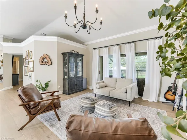 Living room with hanging lights, ornamental molding, light wood-type flooring, and vaulted ceiling