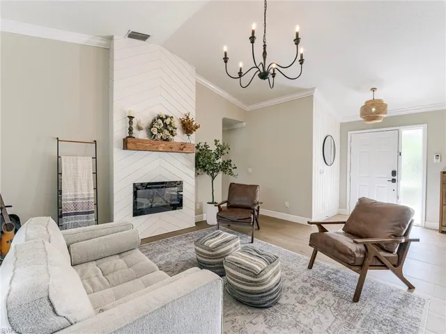 Living room with ornamental molding, a large fireplace, suspended lighting, vaulted ceiling, and light wood-type flooring