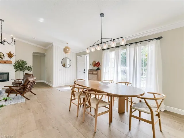Dining area with light wood-style floors, ornamental molding, a glass covered fireplace, and suspended lighting