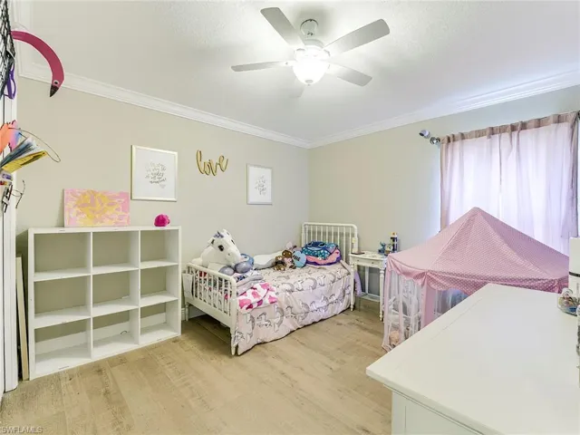 Bedroom featuring light wood-style floors, a ceiling fan, a textured ceiling, and ornamental molding