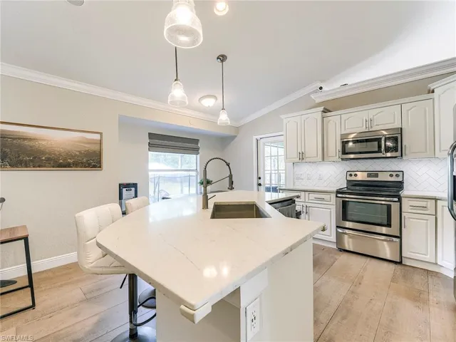 Kitchen with lofted ceiling, a kitchen breakfast bar, stainless steel appliances, ornamental molding, and light wood-style flooring