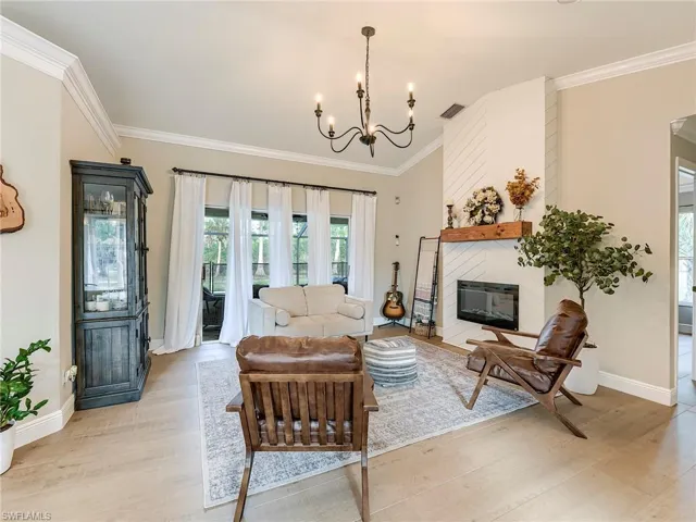 Living area with light wood-type flooring, a fireplace, crown molding, and suspended lighting