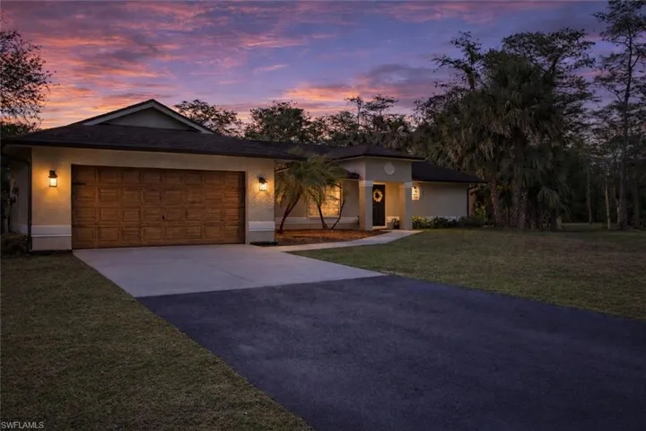 View of front of property featuring driveway, an attached garage, stucco siding, and a yard