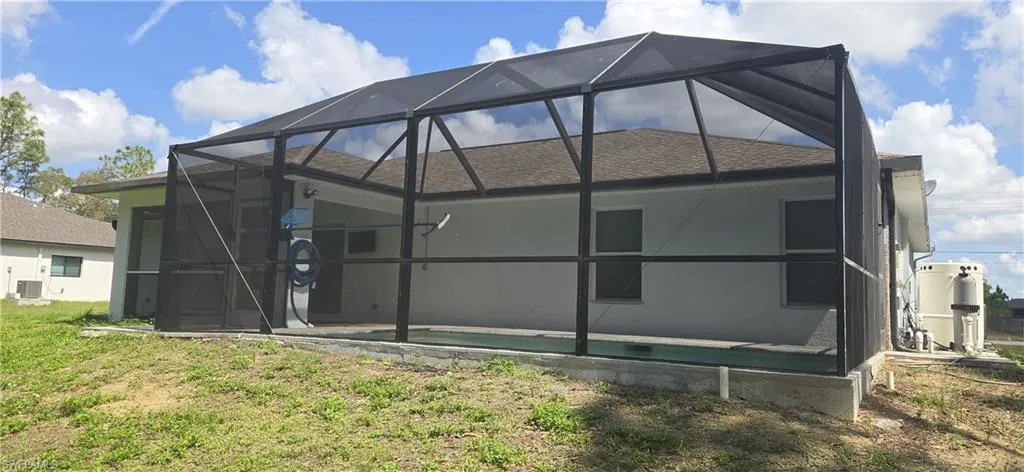 Back of property with glass enclosure, a shingled roof, central AC unit, and stucco siding