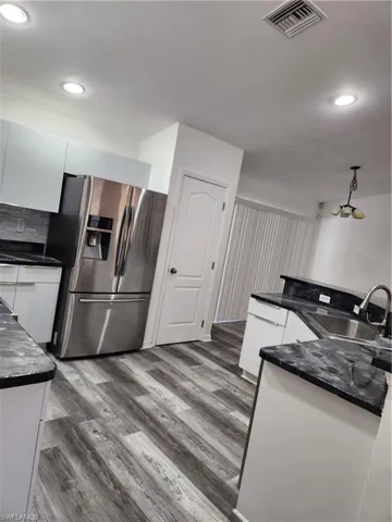Kitchen with refrigerator, a sink, dark countertops, white cabinets, and recessed lighting