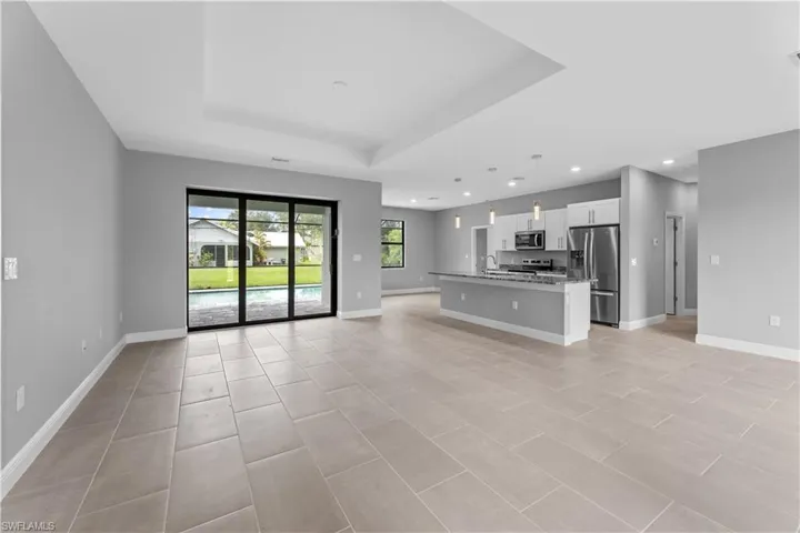 Unfurnished living room featuring sink, light tile flooring, and a raised ceiling
