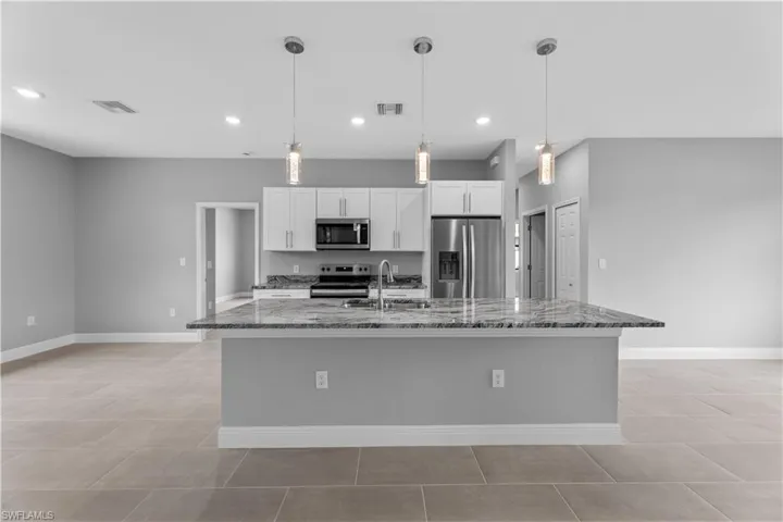 Kitchen with a large island with sink, pendant lighting, light tile floors, and stainless steel appliances