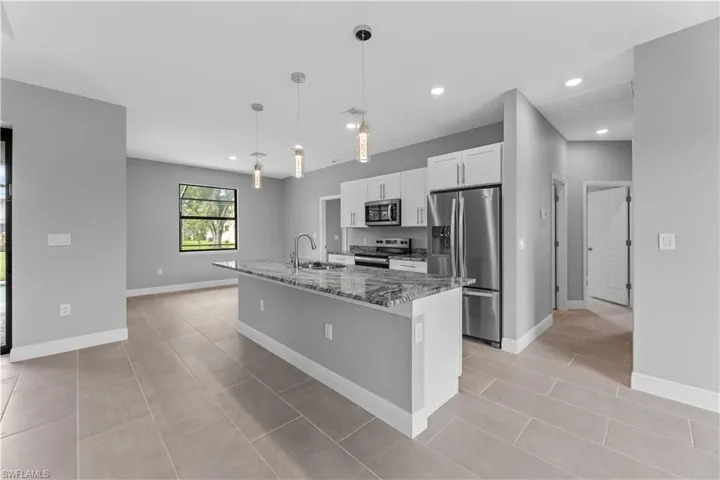 Kitchen featuring a center island with sink, stainless steel appliances, white cabinets, pendant lighting, and light tile flooring