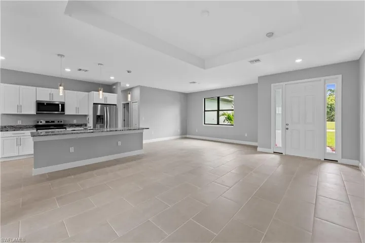 Kitchen featuring stainless steel appliances, an island with sink, a tray ceiling, white cabinets, and pendant lighting