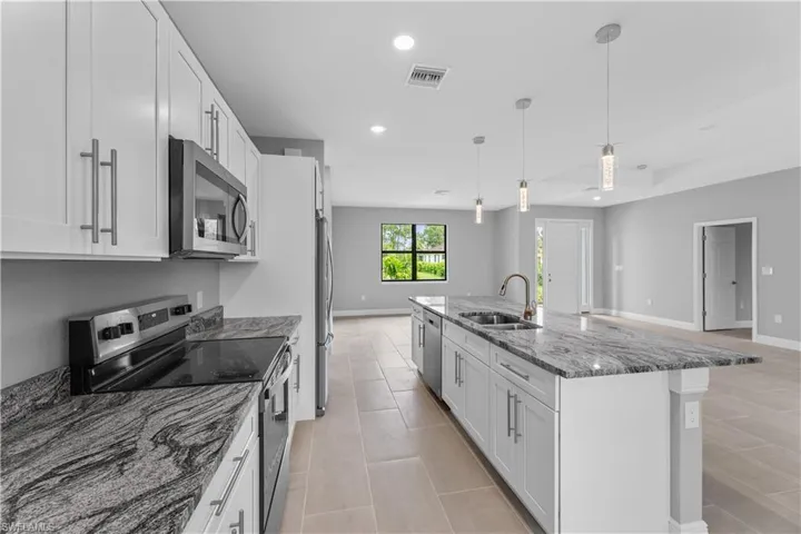 Kitchen featuring appliances with stainless steel finishes, sink, white cabinets, and an island with sink