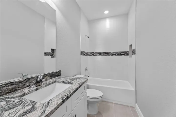 Full bathroom featuring tiled shower / bath combo, tile flooring, toilet, and vanity