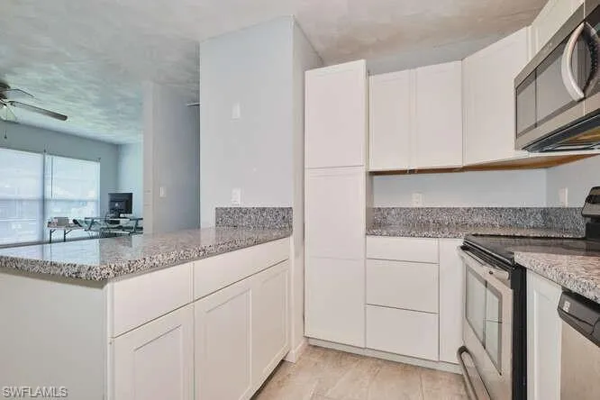 Kitchen featuring appliances with stainless steel finishes, light stone counters, white cabinets, a ceiling fan, and a peninsula