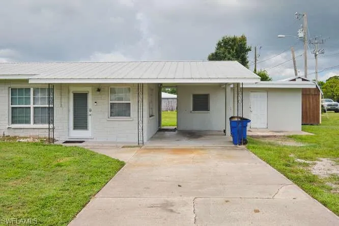 View of front of house featuring a front yard, driveway, a metal roof, an attached carport, and concrete block siding
