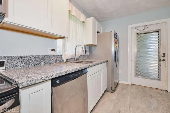 Kitchen featuring appliances with stainless steel finishes, white cabinets, light stone countertops, and light tile patterned floors