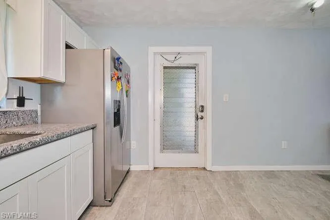 Kitchen featuring white cabinets, light stone counters, and stainless steel refrigerator with ice dispenser