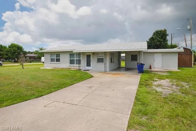 Ranch-style house featuring concrete driveway, an attached carport, and a front lawn