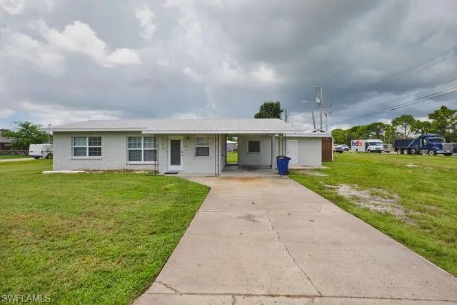 View of front facade featuring a front lawn, a carport, concrete driveway, and a porch