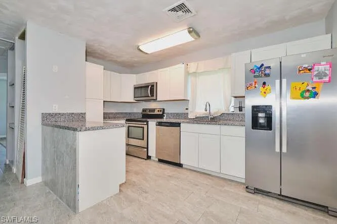 Kitchen with appliances with stainless steel finishes, white cabinetry, and dark stone counters