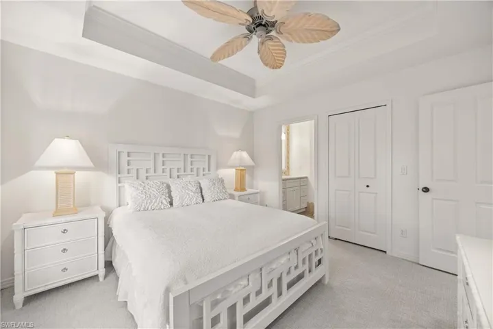 Carpeted bedroom featuring a raised ceiling, ensuite bath, and ceiling fan