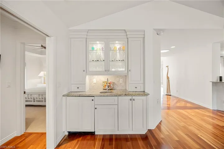 Bar with white cabinets, light hardwood / wood-style flooring, and vaulted ceiling