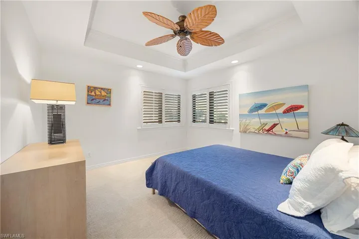 Bedroom featuring a raised ceiling, ceiling fan, light carpet, and ornamental molding