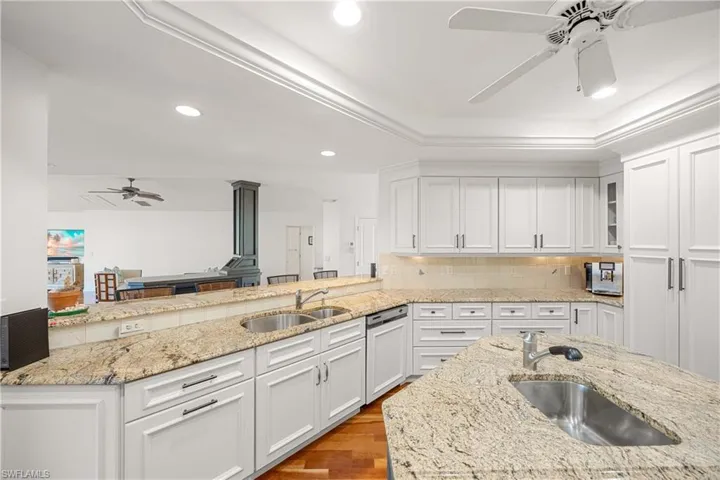 Kitchen with hardwood / wood-style flooring, light stone counters, white cabinetry, and sink