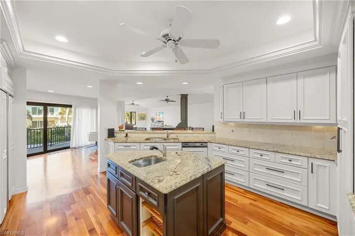 Kitchen with light wood-type flooring, kitchen peninsula, sink, and a tray ceiling