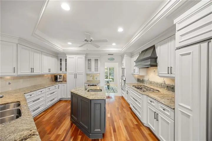 Kitchen with white cabinets, premium range hood, light hardwood / wood-style floors, and an island with sink