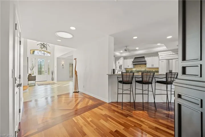 Kitchen with wall chimney range hood, kitchen peninsula, a breakfast bar area, white cabinets, and light wood-type flooring