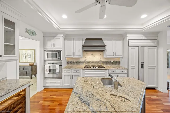 Kitchen featuring sink, built in appliances, light stone countertops, light hardwood / wood-style floors, and custom range hood