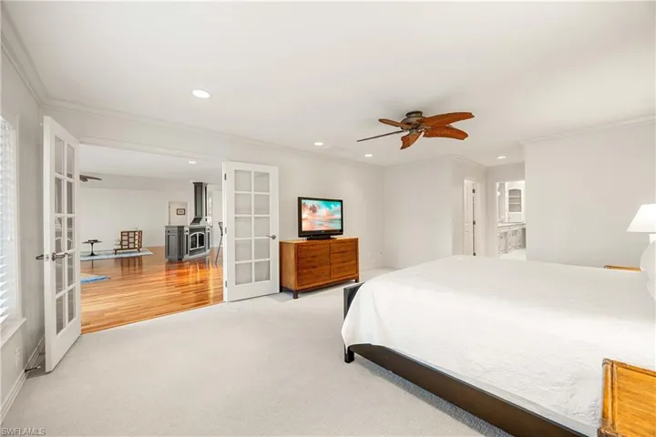 Bedroom with a wood stove, ceiling fan, french doors, light hardwood / wood-style floors, and ornamental molding