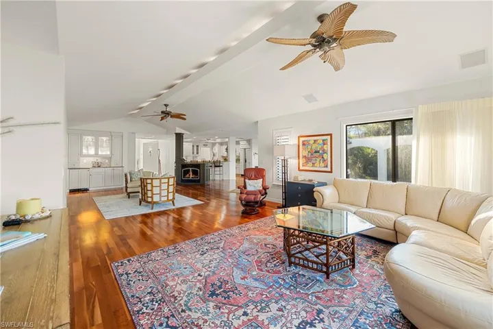 Living room featuring ceiling fan, lofted ceiling with beams, and wood-type flooring