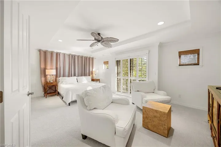 Bedroom featuring ceiling fan, a raised ceiling, light carpet, and crown molding