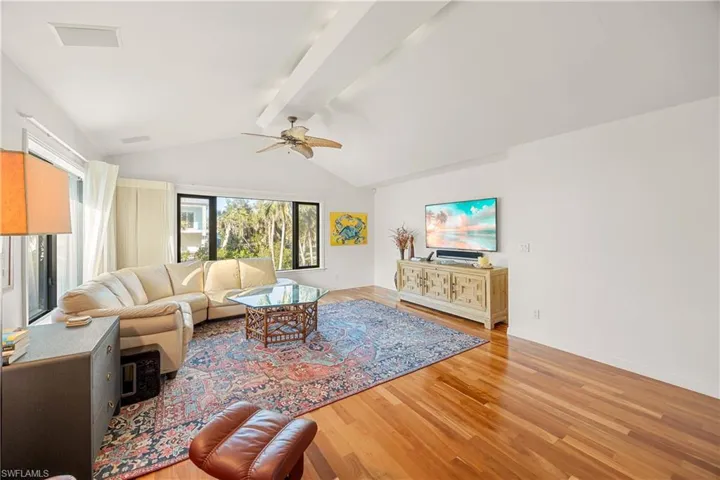Living room with vaulted ceiling with beams, ceiling fan, and wood-type flooring