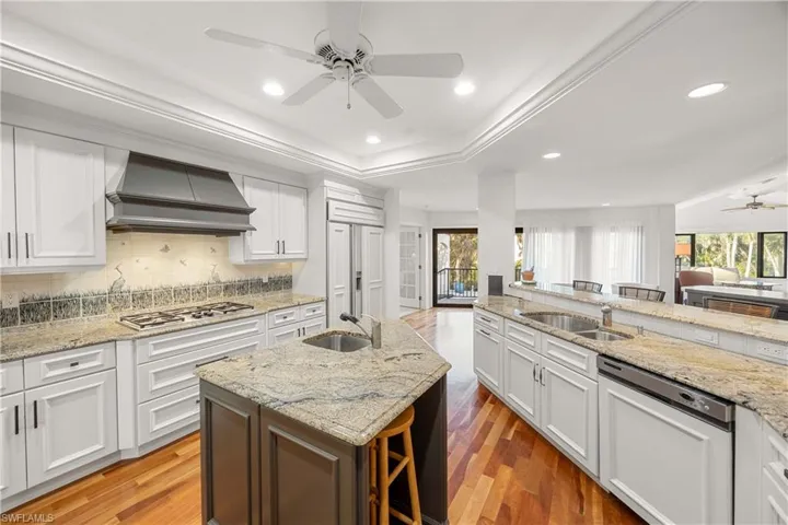Kitchen with hardwood / wood-style flooring, custom range hood, an island with sink, and appliances with stainless steel finishes